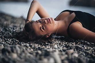 young woman in black skin-tight dress lying on the beach in water