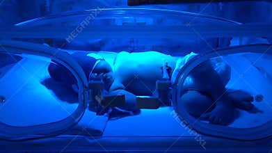 Newborn baby lying in a glass box under the UV lamp.