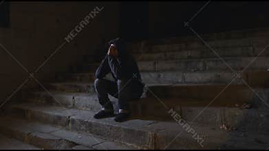 4K video lateral panning 24 fps of young desperate wasted man in hood suffering stress drepression sitting miserable on staircase