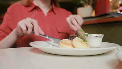 The girl in the cafe eating cheese pancakes with sour cream fork and knife.