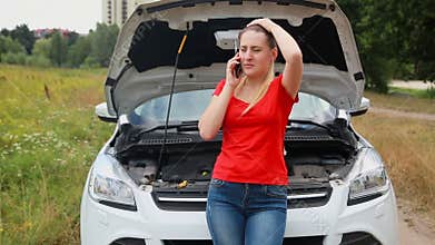 Young frustrated woman leaning on the broken car and calling service for help