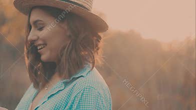 Close-up portrait of a beautiful young girl with long dark hair wearing straw hat. She plays with her hair in the warm