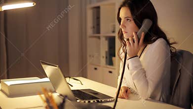 Woman with laptop calling on phone at night office