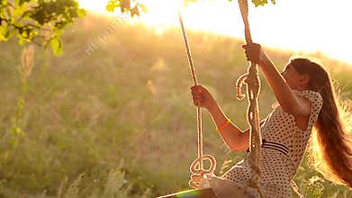 Happy girl swinging on swing in the sun at sunset, hair fluttering in wind