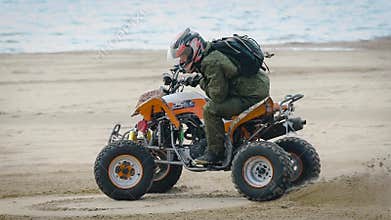 Close up of man in protective equipment and helmet drifting on his ATV on the beach with the sea in the background