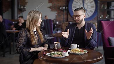 Happy couple of man and woman sitting in cafeteria at the served table with food and beverages spending time together