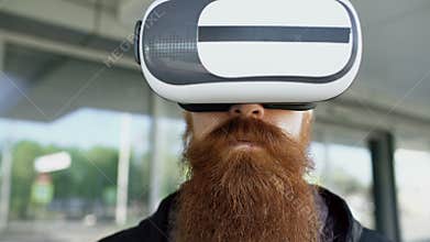 Closeup of Young bearded man using virtual reality headset for 360 VR experience and take of glasses smiling outdoors