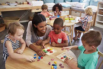 Teacher And Pupils Using Wooden Shapes In Montessori School