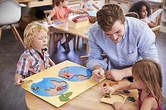 Teacher And Pupils Using Wooden Shapes In Montessori School