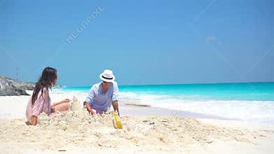 Family with two kids making sand castle at tropical beach