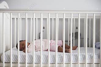 Side View Of Baby Girl Sleeping In Nursery Cot