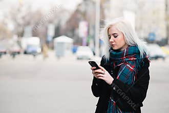 Outdoor portrait of beautiful blonde girl in spring dress enjoying phone middle of the city. Walk around the city.