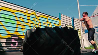 Handsome sportsman with bare torso training with hammer on the street