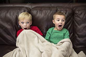 Two scared little boys sitting on a couch watching TV