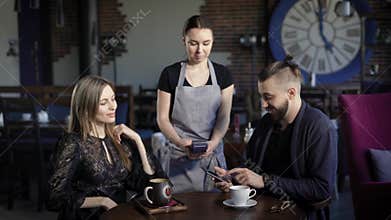 Couple paying with phone for dinner. Young couple sitting in restaurant and male paying for dinner with phone.