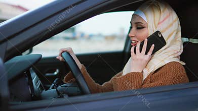 Modern Muslim woman having a phone talk at the wheel