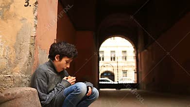 A homeless teenager eating a crust of bread in a gateway against the background of a grate