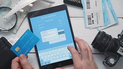 Top view traveler`s hands paying for airplane tickets on line using digital tablet and credit card at white wooden desk