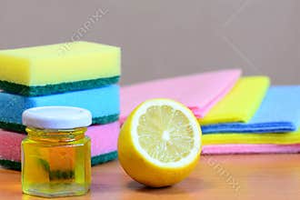 Cleaning sponge with scrub and rags set, olive oil in glass jar, lemon half on a wooden table. Eco house cleaning set. Closeup