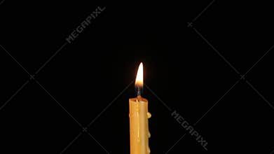 Thin wax candle burning on a black background. Close-up.