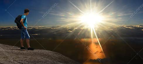 Man on sunshining rock above stormy clouds. Panorama