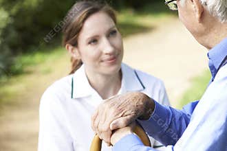Senior Man's Hands Resting On Walking Stick With Care Worker In