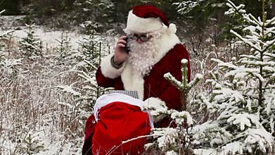 Santa Clause with smartphone near gift bag in the snowy woods