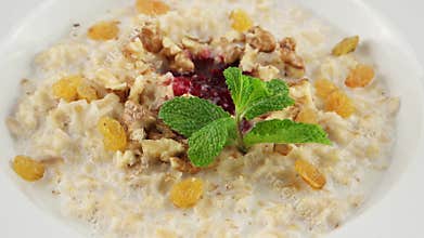 Healthy breakfast, oatmeal porridge, raisins, walnuts and milk (loop)