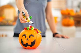 Woman putting trick or treat candy in halloween bucket. Closeup