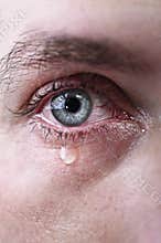 Close up of blue eye of man crying in tears sad and full of pain in depression