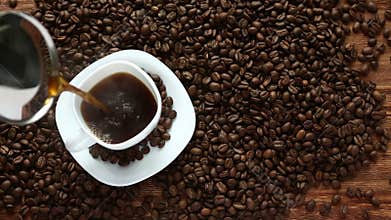 Pouring coffee in cup surrounded by coffee beans