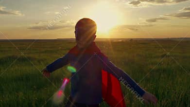Boy superhero in a field at sunset