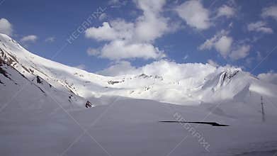 Snow-covered mountains in the background of clouds and blue sky from a car window. Caucasus, Georgia.