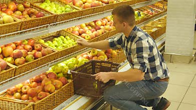 Man selecting fresh red apples in grocery store produce department and putting it in the basket. Handsome guy is