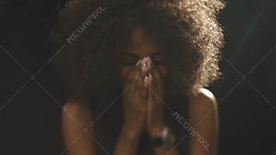 Sad beautiful african woman looking down and covers face by hands