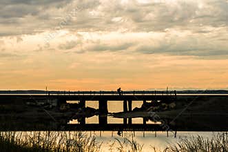 Man bicycling over a railroad trestle on cloudy sunset evening.