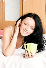 Cheerful girl with a cup of coffee in bed