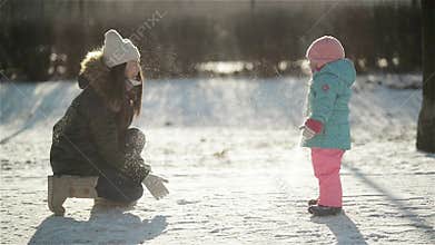 Laughing Woman in Warm Clothing is Throwing Snow at Her Daughter Wearing Snowsuit. Mother and Child Enjoying Cold Sunny