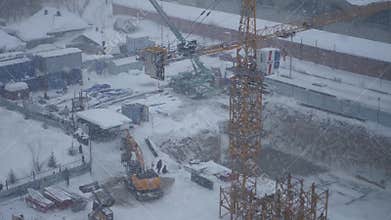 Excavator and a crane working on a construction site during a snow blizzard, 4k