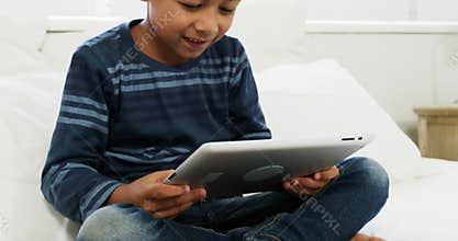 Boy using digital tablet while relaxing on bed