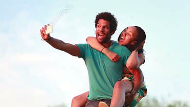 Young man giving his girlfriend a piggyback ride while taking selfie