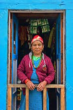 Nepalese Sherpa woman in traditional attire standing at front blue door along Everest Base Camp village, Nepal