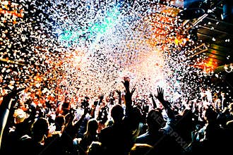 Silhouettes of concert crowd in front of bright stage lights with confetti