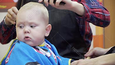 Little boy cuts the barber. He sits in a chair that looks like a car. Mom it distracts and plays with him. Head close-up