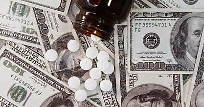Lots of dollar bank notes scattered with pills on table