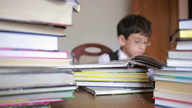 Boy sitting at a table with a stack of books. child reading. boy with glasses