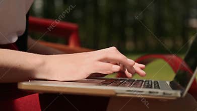 Closeup of girl`s hands on the laptop. Girl typing, using laptop outdoors.