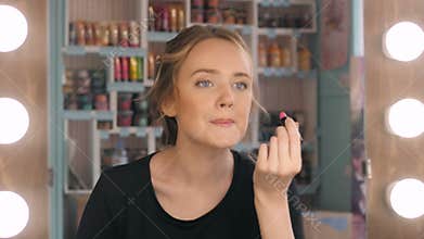 Woman putting red lipstick looking in mirror. Makeup at night getting ready before going to party.