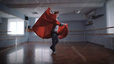 The young man in the rehearsal hall. Rehearses dance for statement. He by means of red fabric does rotations. Fabric