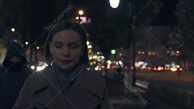 Frightened lady is followed be thief in hood on dark city street, urban crime